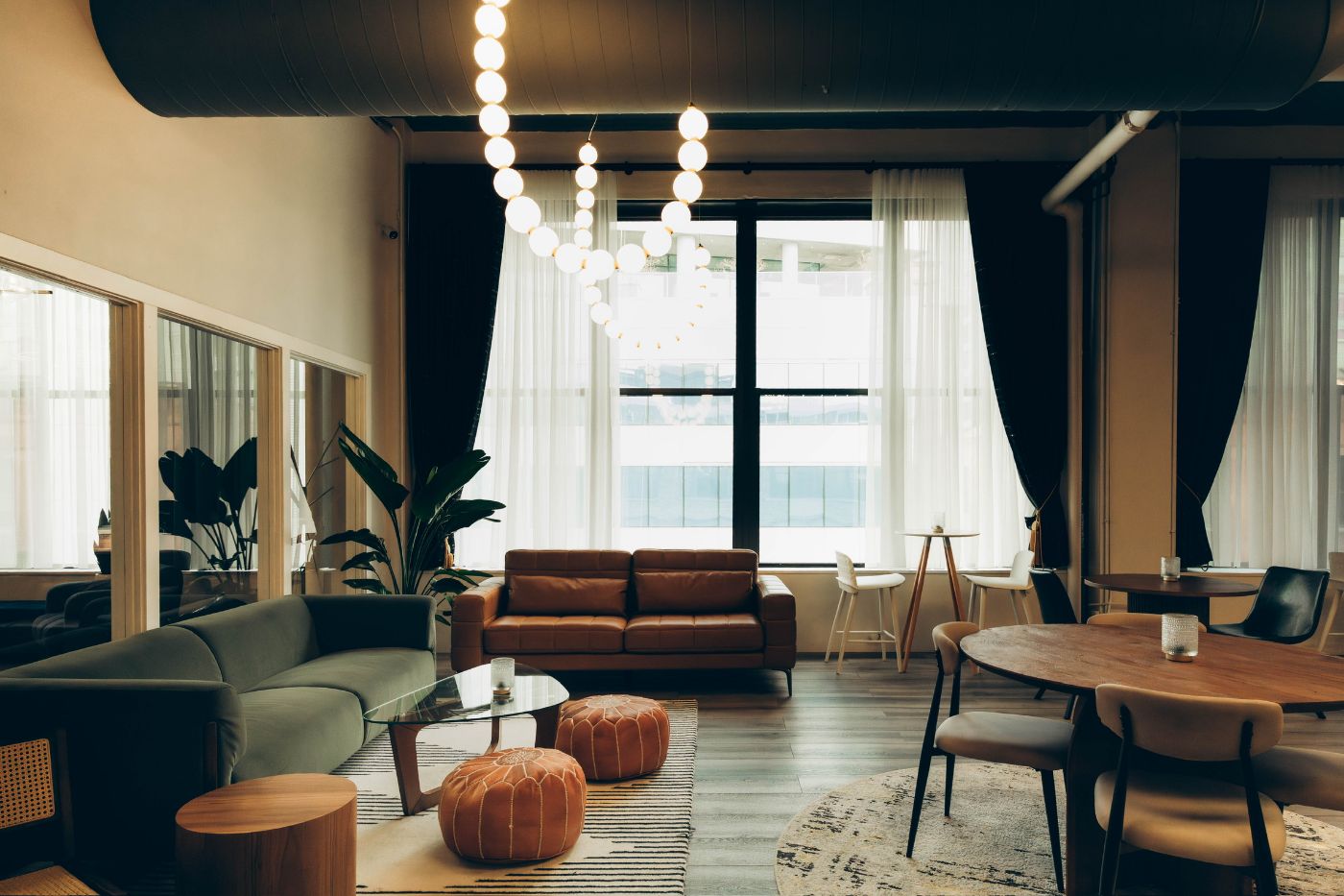 The Three Cities Social lounge at golden hour — velvet and leather sofas, pearl-string chandelier, floor-to-ceiling windows