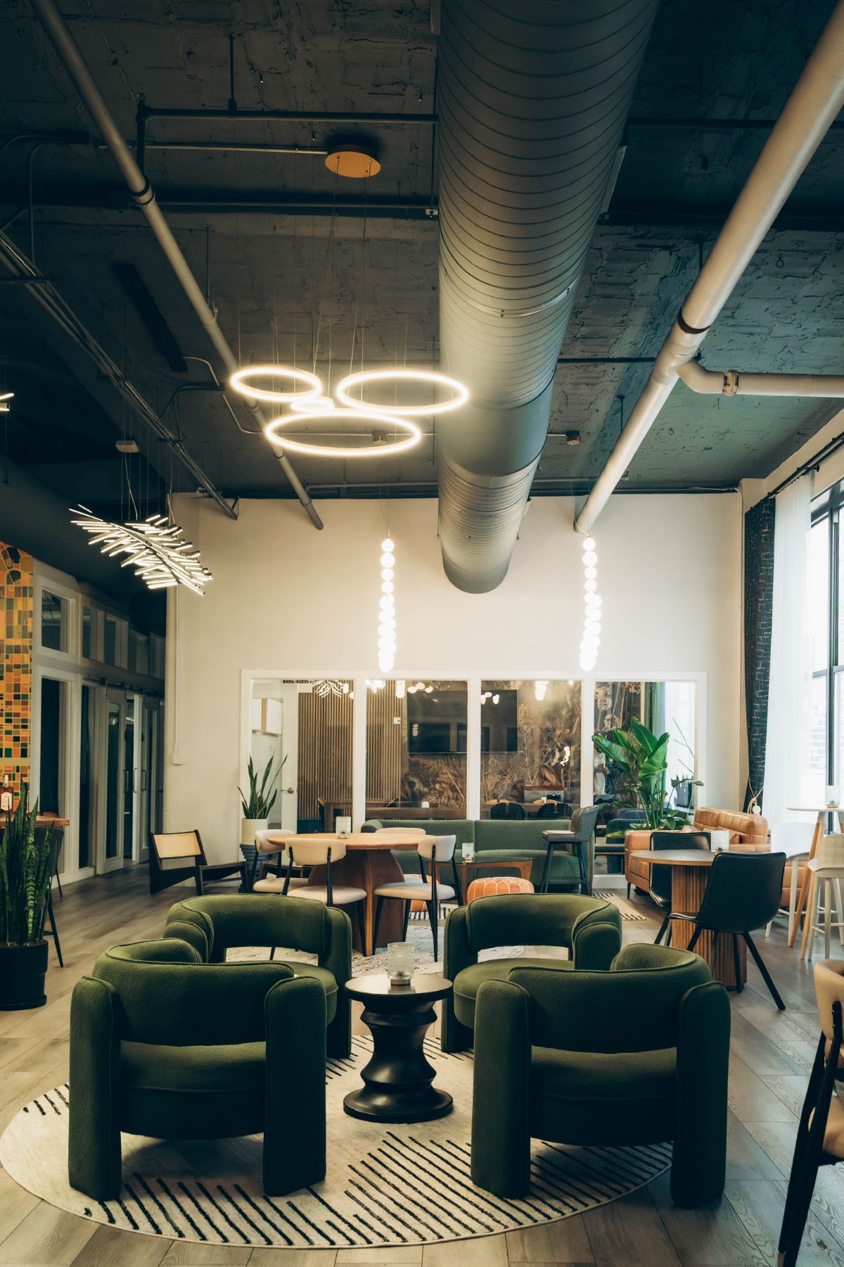 The Three Cities Social clubhouse floor — green lounge chairs in a circle, ring chandeliers, coworking tables beyond