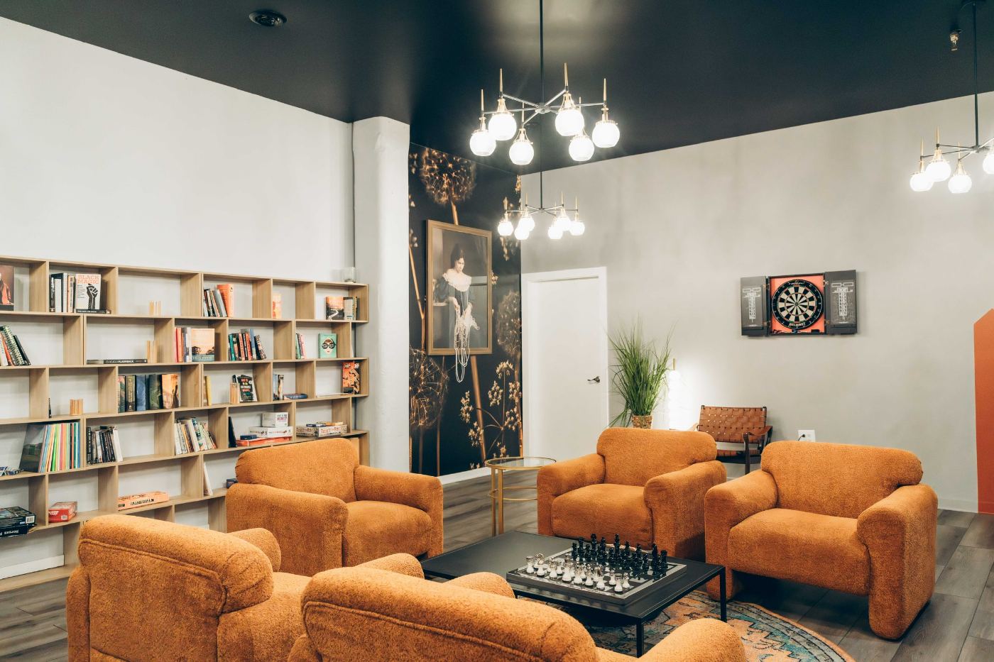 The Three Cities Social library and games room — bookshelves, orange armchairs, a chess set mid-game